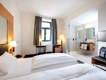 Ein gemütliches Bett steht der Mitte einer Suite. Das Zimmer hat ein Badezimmer mit Glaswänden und einen Tür ins zweite Zimmer.