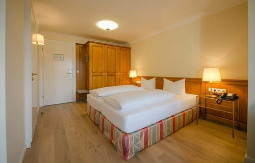 A covered double bed stands in the middle of the hotel room, next to it is a large wardrobe