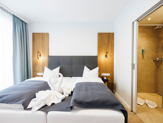 Das Doppelbett im Apartment Komfort Plus worauf aus Handtüchern zwei Schwäne die ein Herz zeigen gefaltet sind.