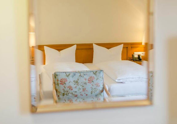 Das Doppelbett und der Blumen-Stuhl spiegeln sich im Spiegel.