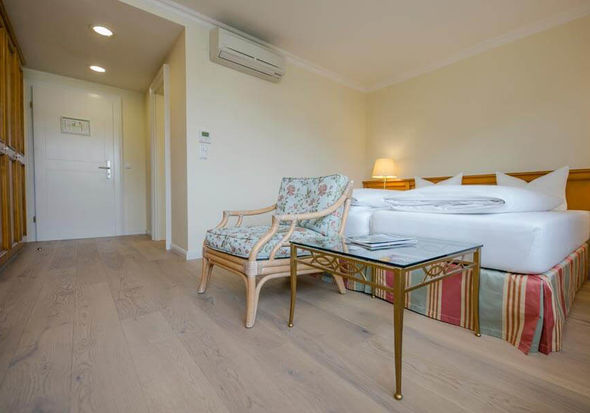 Ein Blumenstuhl mit dazugehörigen Glastisch steht vor dem Doppelbett.