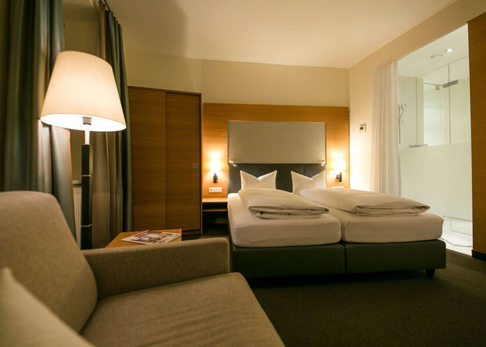 View into the business room of the Hotel Sailer with a double bed, a comfortable sofa and a floor lamp