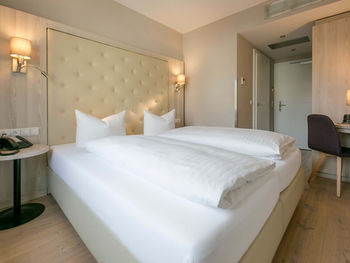 Vista nella camera doppia Basic dell'Hotel Sailer con un grande letto matrimoniale, lenzuola bianche, una scrivania e una sedia