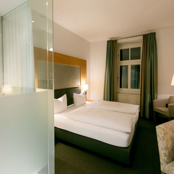 View into the business room of Hotel Sailer with a double bed, a comfortable sofa and a floor lamp