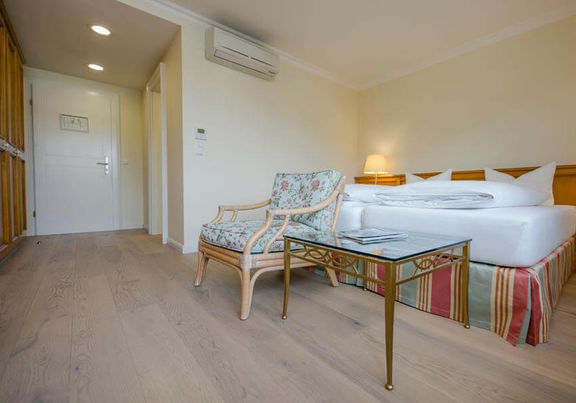 Ein Blumenstuhl mit dazugehörigen Glastisch steht vor dem Doppelbett.