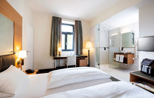 Ein gemütliches Bett steht der Mitte einer Suite. Das Zimmer hat ein Badezimmer mit Glaswänden und einen Tür ins zweite Zimmer.