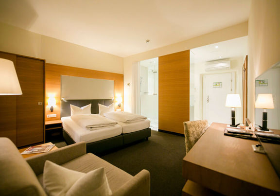 View into the business room of the Hotel Sailer with a double bed, a comfortable sofa and a floor lamp