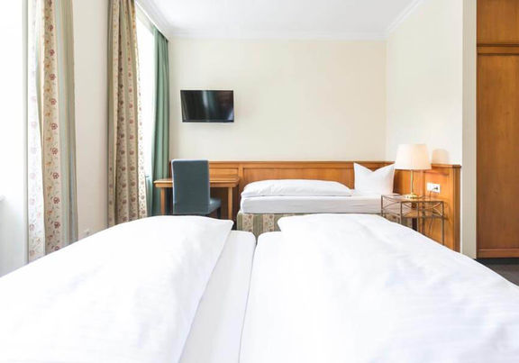 Blick in das Dreibettzimmer mit einem Doppelbett und einem Einzelbett, sowie einem Schreibtisch und einem Fernseher