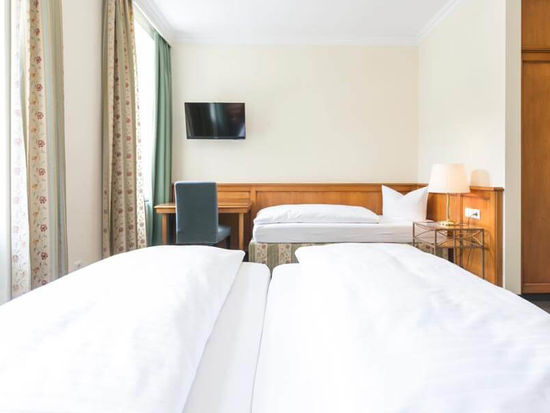 Blick in das Dreibettzimmer mit einem Doppelbett und einem Einzelbett, sowie einem Schreibtisch und einem Fernseher