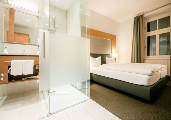 Blick in das Businesszimmer des Hotel Sailer mit einem Doppelbett und einem großen Badezimmer mit Dusche