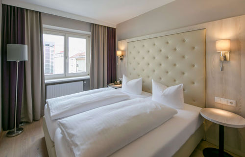 View of the Basic double room at Hotel Sailer Innsbruck with a double bed, a floor lamp, parquet flooring and a large window.