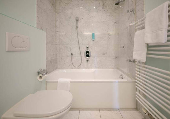 Das helle Marmorbadezimmer bezieht ein WC, eine Badewanne mit Duschglas und einen Heizkörper für nasse Handtücher.