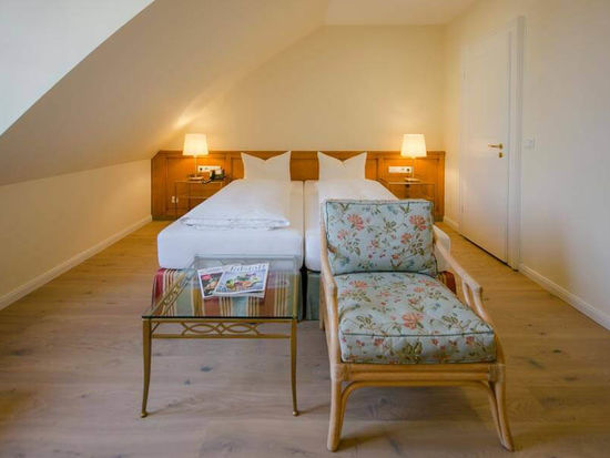 Ein Blumenstuhl mit dazugehörigen Glastisch steht vor dem Doppelbett.