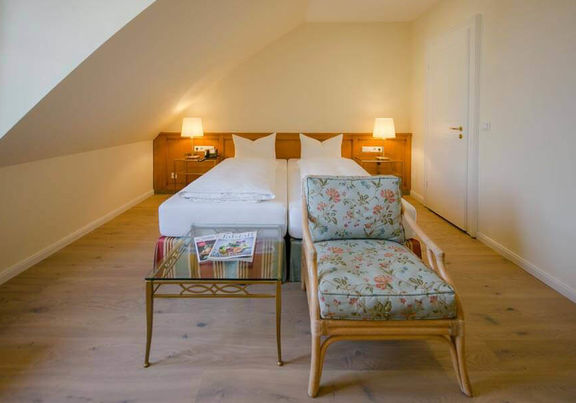 Ein Blumenstuhl mit dazugehörigen Glastisch steht vor dem Doppelbett.