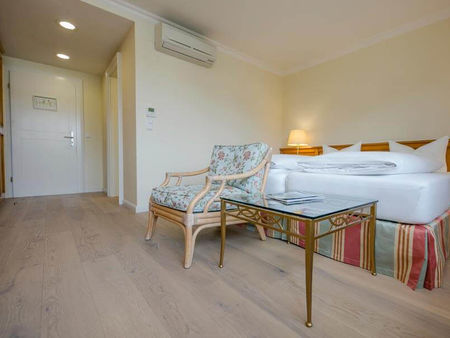 Ein Blumenstuhl mit dazugehörigen Glastisch steht vor dem Doppelbett.