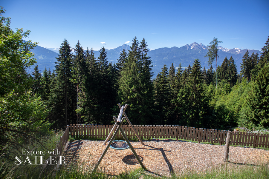 Kleiner Spielbereich bei der Umbrüggler Alm mit Blick auf Wald und die Tiroler Bergwelt.