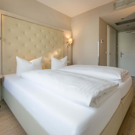 Blick in das Doppelzimmer Basic im Hotel Sailer mit einem großen Doppelbett, weißer Bettwäsche, einem Schreibtisch und einem Stuhl