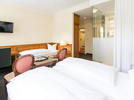 Blick in das Dreibettzimmer mit einem Doppelbett und einem Einzelbett, sowie einem Schreibtisch und einem Fernseher