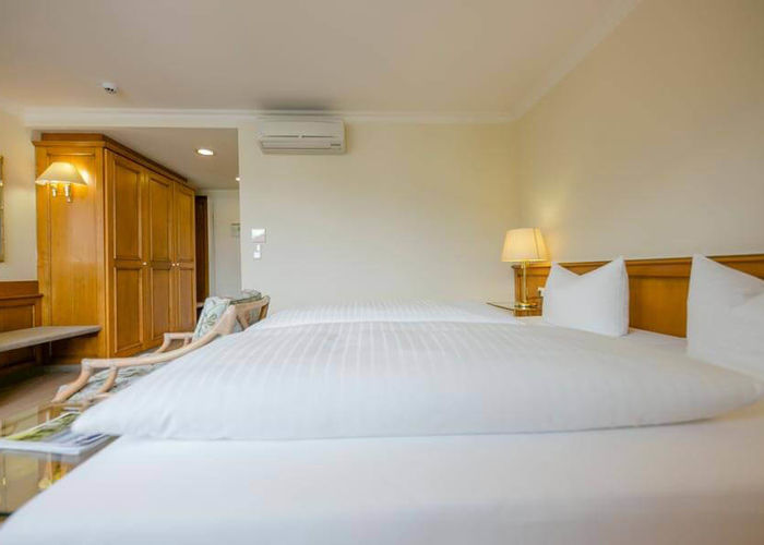 Soft double beds are located in a spacious hotel room. There is a large wardrobe and a seating area in the room.