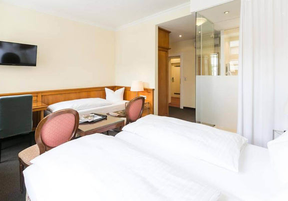 Blick in das Dreibettzimmer mit einem Doppelbett und einem Einzelbett, sowie einem Schreibtisch und einem Fernseher