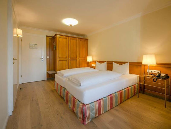 Ein bezogenes Doppelbett steht in der Mitte des Hotelzimmers, daneben ist ein großer Kleiderschrank