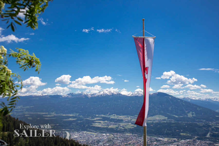 Österreichische Fahne mit Blick über Innsbruck, das Inntal und die umliegenden Alpen von der Höttinger Alm.