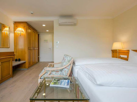 Ein Stuhl steht vor dem Doppelbett neben einen Glastisch. Im Raum befindet sich eine Kommode und ein großer Schrank.