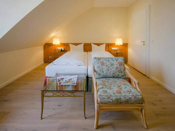 Ein Blumenstuhl mit dazugehörigen Glastisch steht vor dem Doppelbett.