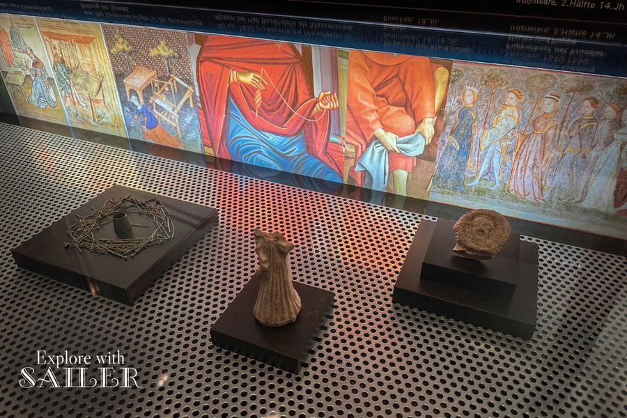 Historic artefacts and medieval illustrations displayed in an exhibition case at the Hall Mint in Tirol.
