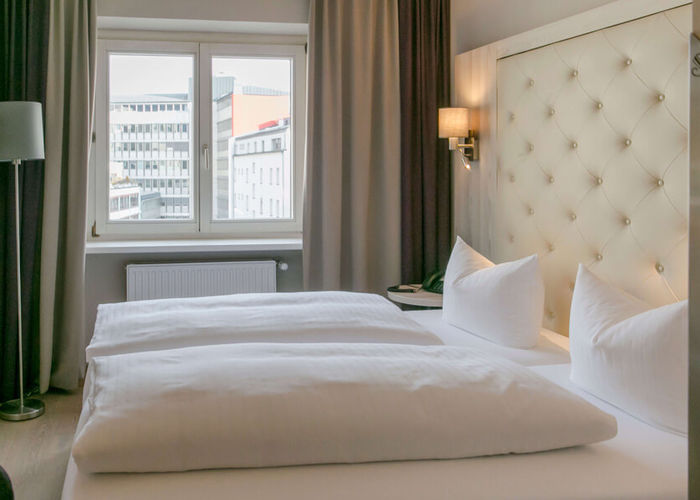 View into the double room Basic at Hotel Sailer Innsbruck with a double bed, a floor lamp, parquet floor and a large window