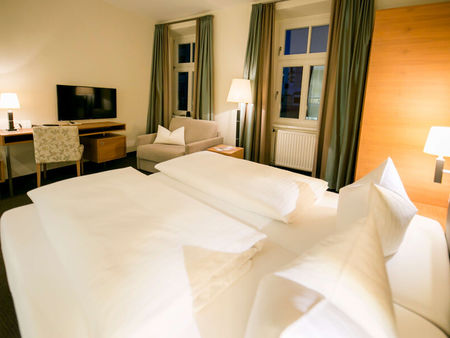 Vista nella camera business dell'Hotel Sailer con un letto matrimoniale, un comodo divano, una lampada da terra e una TV a schermo piatto