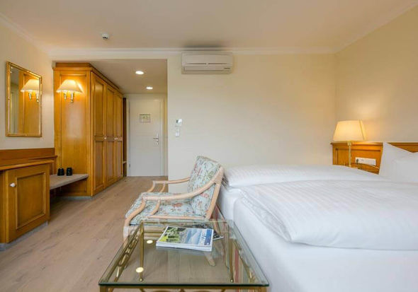 Ein Stuhl steht vor dem Doppelbett neben einen Glastisch. Im Raum befindet sich eine Kommode und ein großer Schrank.