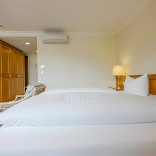 Soft double beds are located in a spacious hotel room. There is a large wardrobe and a seating area in the room.