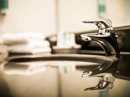 Eine silberne Armatur spiegelt sich auf den sauberen, schwarzen Waschbecken wieder.