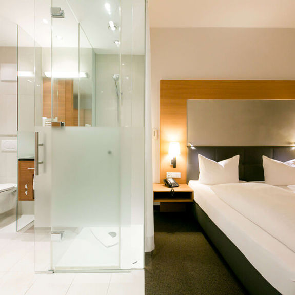 View into the business room of the Hotel Sailer with a double bed and a large bathroom with shower