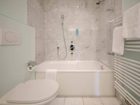 Das helle Marmorbadezimmer bezieht ein WC, eine Badewanne mit Duschglas und einen Heizkörper für nasse Handtücher.