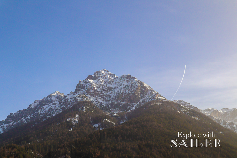 Schneebedeckte Berggipfel ragen über bewaldeten Hängen unter klarem Himmel entlang der Strecke ins Stubaital.