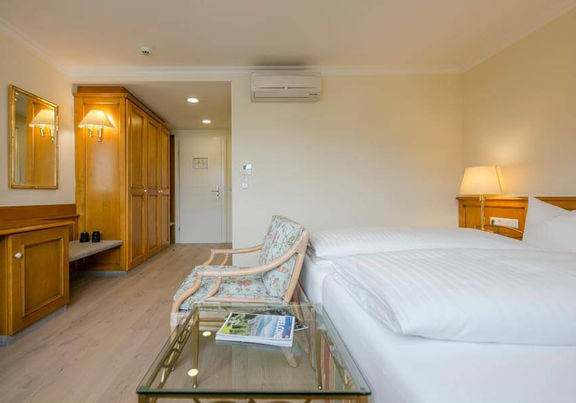 Ein Stuhl steht vor dem Doppelbett neben einen Glastisch. Im Raum befindet sich eine Kommode und ein großer Schrank.