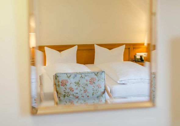 Das Doppelbett und der Blumen-Stuhl spiegeln sich im Spiegel.