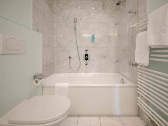 Das helle Marmorbadezimmer bezieht ein WC, eine Badewanne mit Duschglas und einen Heizkörper für nasse Handtücher.