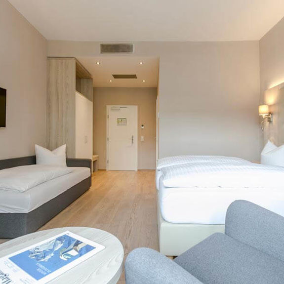 A double bed and a single bed with a bright illuminated hotel room