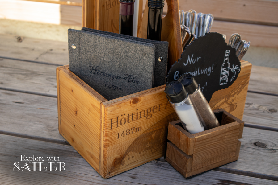 Holztisch mit Speisekarte, Gewürzen und einem Hinweis, dass in der Höttinger Alm ausschließlich Barzahlung möglich ist.