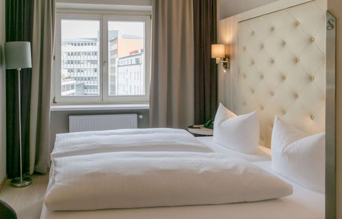 View into the double room Basic at Hotel Sailer Innsbruck with a double bed, a floor lamp, parquet floor and a large window