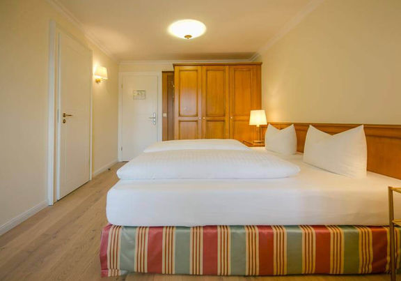 Ein bezogenes Doppelbett steht in der Mitte des Hotelzimmers, daneben ist ein großer Kleiderschrank