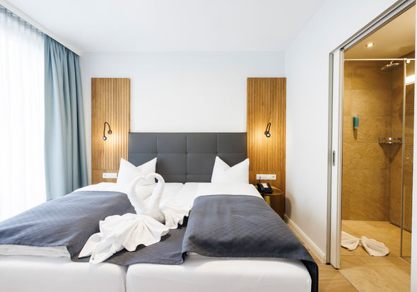 Das Doppelbett im Apartment Komfort Plus worauf aus Handtüchern zwei Schwäne die ein Herz zeigen gefaltet sind.