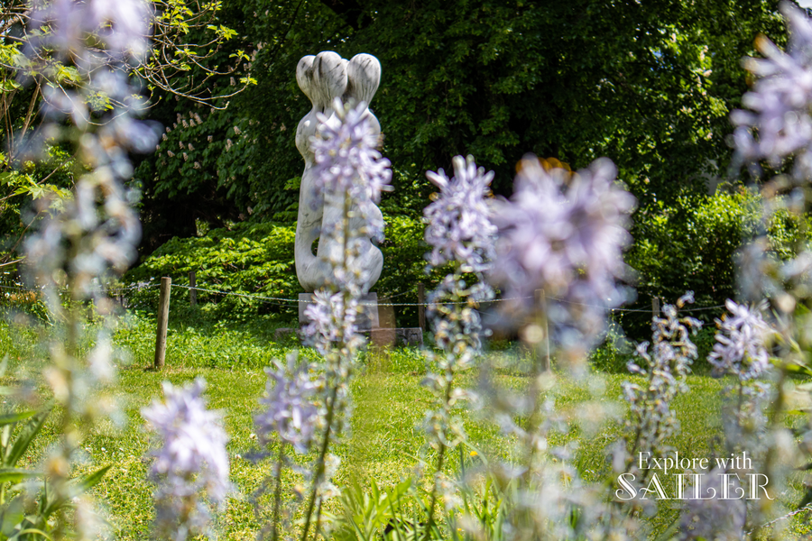 Steinskulptur umgeben von blühenden Pflanzen und grünen Bäumen im Botanischen Garten.