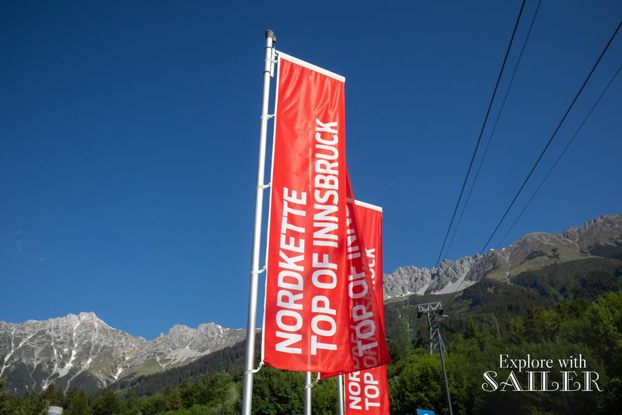 Rote Nordkette-Fahnen wehen vor einer beeindruckenden Bergkulisse und blauem Himmel in Innsbruck.