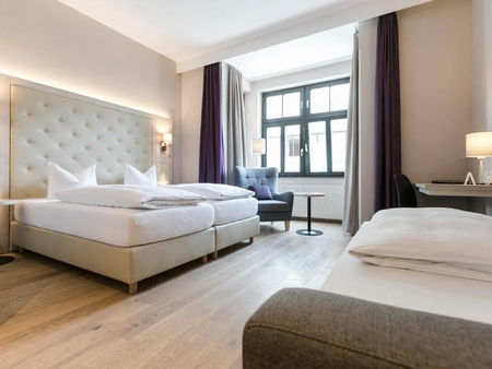 Ein Doppelbett und ein Einzelbett mit einer hellen Sitzgelegenheit am Fenster und einen feinen Schreibtisch