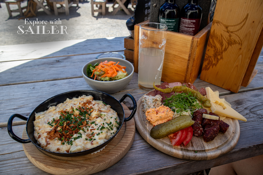 Traditionelle Tiroler Gerichte und regionale Jause auf einem Holztisch auf der Sonnenterrasse der Höttinger Alm.