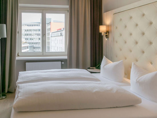 Vista nella camera doppia Basic dell'Hotel Sailer Innsbruck con un letto matrimoniale, una lampada da terra, pavimento in parquet e una grande finestra